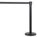 A black metal Lancaster Table & Seating crowd control stanchion with black retractable belt.