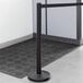 A Lancaster Table & Seating black metal crowd control stanchion with black retractable belt.