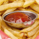 Stainless steel oval sauce cup filled with ketchup on french fries.