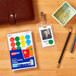 A package of Avery round removable labels in assorted colors on a table with a wallet, badge, and pencils.