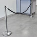 A Lancaster Table & Seating black stanchion with silver ends and rope tied to it.