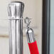 A close-up of a Lancaster Table & Seating red stanchion pole with silver ends and a red rope.