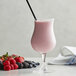 A glass of pink Monin Wildberry Fruit Smoothie with a straw and berries.