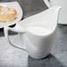 A white porcelain creamer with a handle on a table with food.