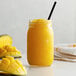 A glass jar of Monin Mango Fruit Smoothie Mix with a straw in it.