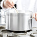A person stirring a Vollrath Wear-Ever Classic Select sauce pot on a kitchen counter.