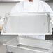 A chef using a Vollrath stainless steel food transport cover on a large pan.