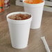 Two Dart white foam cups filled with orange juice and ice on a wood surface.