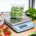 An Edlund BRAVO! digital portion scale on a counter with a bag of greens on it.