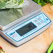 An Edlund Bravo digital portion scale with a ClearShield cover on a counter with a bag of greens on top.