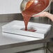A person pouring brown liquid into an Ateco rectangular cake pan on a counter.
