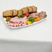 A plate of meat, bread, and vegetables on a table with a Hoffmaster white paper table cover.