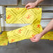 A person holding a yellow Spilfyter absorbent pad with a warning sign on it.