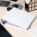 An Avery white heavy-duty view binder on a desk with papers inside.