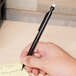 A hand using a Universal Smoke Barrel mechanical pencil to write on a sticky note.