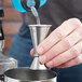 A person using an American Metalcraft stainless steel jigger to pour liquid into a metal cup.