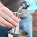 A hand using an American Metalcraft stainless steel Japanese style jigger to pour liquid into a metal container.