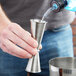 A person pouring liquid into an American Metalcraft stainless steel jigger.