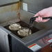 A hand using tongs to lower a Tablecraft Tortilla Double Taco Fry Basket into a fryer.