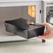 A hand holding a Choice black folded paper take-out box in a home kitchen microwave.