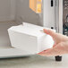 A hand holding a small white folded paper take-out box.