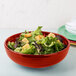A Fiesta Scarlet china bistro bowl filled with salad on a table.