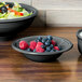 A Fiesta Slate china bowl filled with berries and salad on a table with more bowls of fruit and salad.