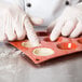 A gloved hand presses white dough into a Matfer Bourgeat orange silicone tartlet mold.