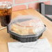 A Solo black plastic take-out container with food inside, a clear lid, a drink, and a plastic fork on a table.