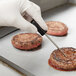 A gloved hand uses a Cooper-Atkins DuraNeedle probe to check the temperature of meat patties.