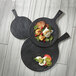 An American Metalcraft round melamine serving paddle with black faux slate on a wood table with black plates of food.