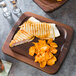 An American Metalcraft wooden serving board with a grilled cheese sandwich and potato chips.