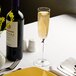 A bottle of wine sits on a table next to a Stolzle New York flute glass filled with champagne.