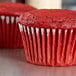 A close-up of a red velvet cupcake in a Hoffmaster white fluted baking cup.