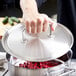 A person holding a Vollrath stainless steel lid over a pot of beans.