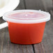 A Newspring oval plastic souffle container filled with red liquid on a table.
