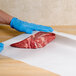 A person in blue gloves wrapping a piece of meat in Choice white freezer paper.