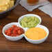 A three-tiered white bowl with three sections holding guacamole, salsa, and yellow liquid.