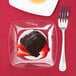 A piece of chocolate cake with strawberries on a Fineline clear plastic dessert plate next to a fork.