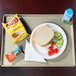 A Cambro Cameo yellow dietary tray with a sandwich, tomatoes, chips, and a drink on it.
