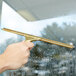 A hand using a Unger GoldenClip brass squeegee handle to clean a window.