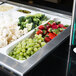 A white Cambro food pan with broccoli, strawberries, and other fruits and vegetables.