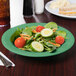 A rainforest green melamine bowl with a salad of tomatoes, cucumbers, and carrots.