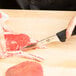 A person using a Victorinox Stiff Narrow Boning Knife with a black handle to cut meat.