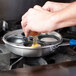 A person cooking a Vollrath Wear-Ever aluminum egg poacher cup in a pan on a stove.
