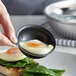 A close up of a pan with a Vollrath Wear-Ever non-stick aluminum egg poacher cup with eggs in it.