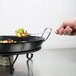 A hand using an American Metalcraft wrought iron griddle stand to cook vegetables on a griddle.