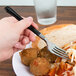 A person using a WNA Comet Reflections Duet stainless steel look plastic fork with a black handle to eat food.