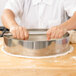 A person using an American Metalcraft stainless steel dough cutting ring to cut dough in a metal bowl.