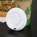 A white Eco-Products recycled content paper hot cup lid on a coffee cup on a table with a donut with sprinkles.